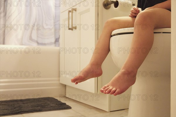 Legs of toddler girl (2-3) sitting on toilet seat