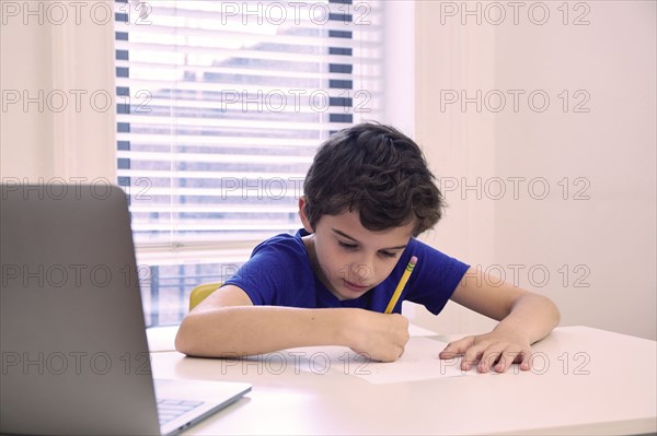 Boy (8-9) writing test at during remote lesson at home