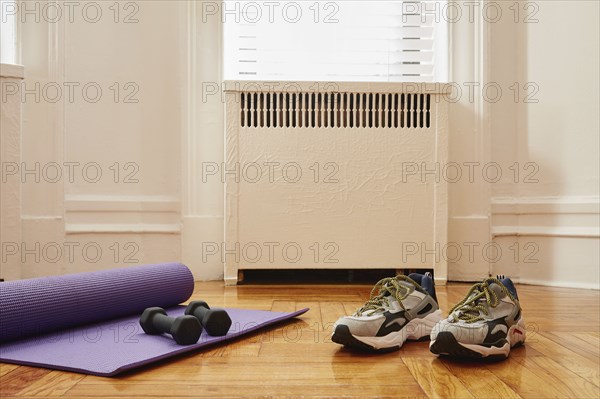 Yoga mat, weights and sports shoes on floor at home gym