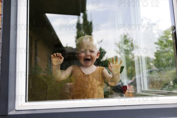 Baby boy (18-23 months) standing behind window and crying