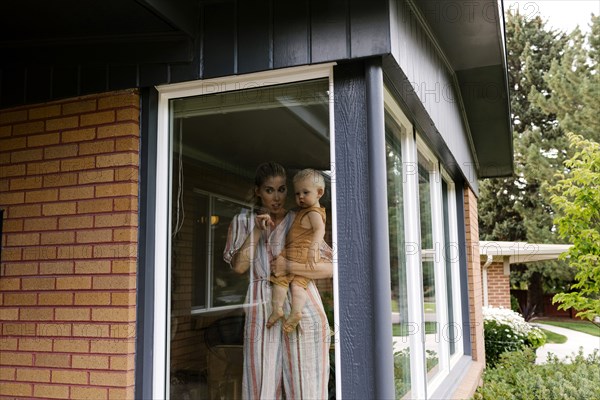 Mother with baby son (18-23 months) standing behind window