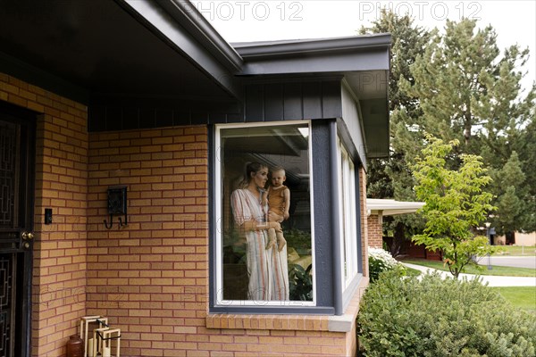 Mother with baby son (18-23 months) standing behind window