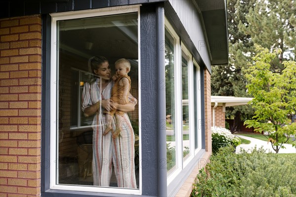 Mother with baby son (18-23 months) standing behind window
