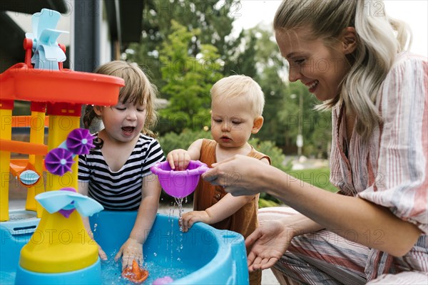 Mother with baby son (18-23 months) and toddler daughter(2-3)playing with water in garden