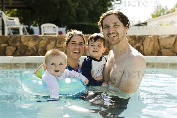 Portrait of parents with kids (2-3, 6-11 months ) standing in outdoor swimming pool