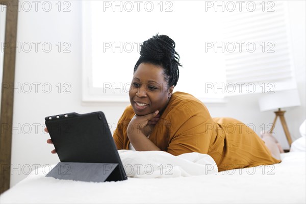 Smiling woman lying on bed and using tablet