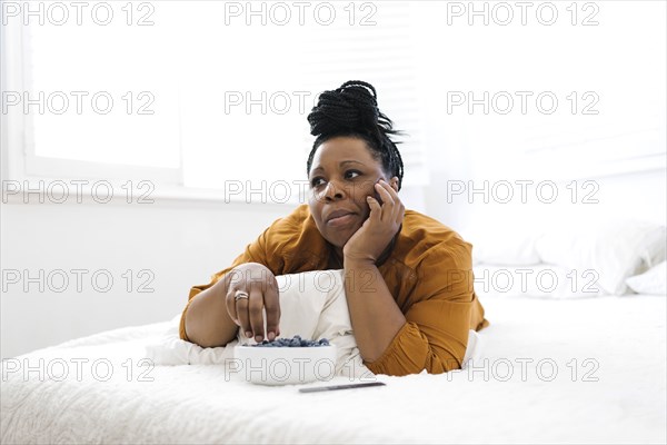 Woman lying on bed, eating blueberries and watching tv