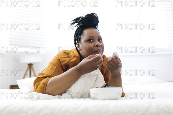 Woman lying on bed, eating blueberries and watching tv