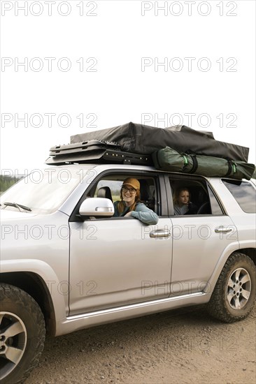 Smiling woman with daughter (6-7) sitting in off road car with tent on roof