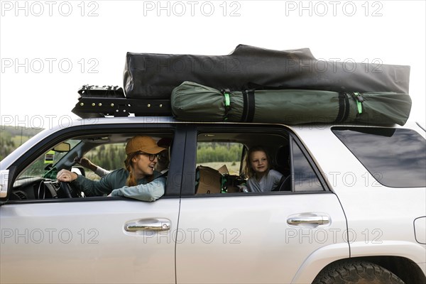 Smiling woman with daughter (6-7) sitting in off road car with tent on roof