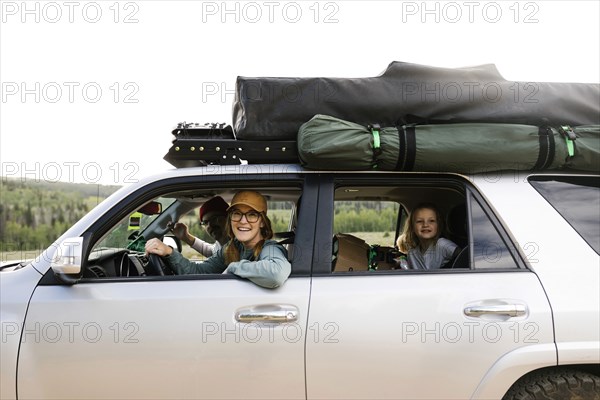 Parents with daughter (6-7) sitting in off road car with tent on roof