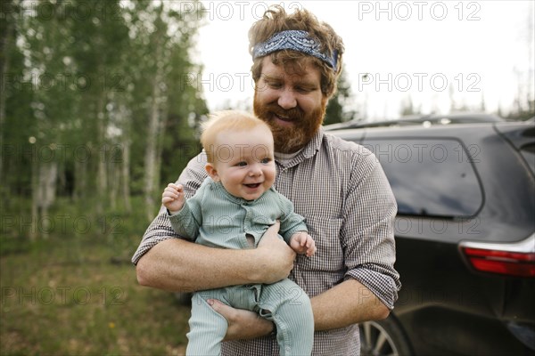 USA, Utah, Uinta National Park, Smiling man holding baby son (6-11 months) in field, car in background