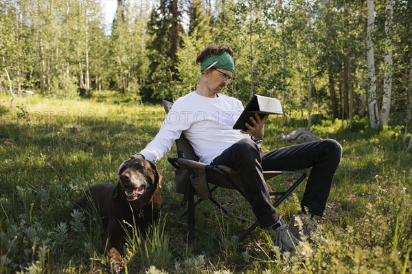 USA, Utah, Uinta National Park, Man with dog sitting in meadow in forest, using tablet