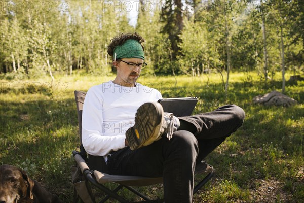 USA, Utah, Uinta National Park, Man with dog sitting in meadow in forest, using tablet