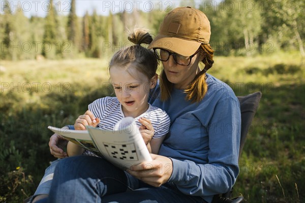 USA, Utah, Uinta National Park, Mother and daughter (6-7) doing crossword in meadow in forest