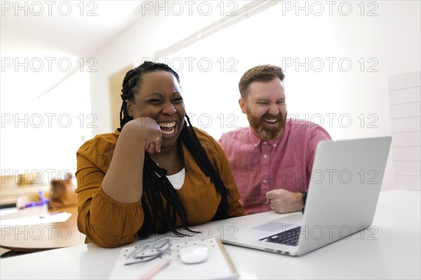 Smiling man and woman looking at laptop at desk in home office