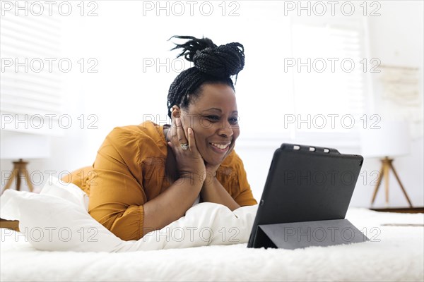 Smiling woman lying on bed and looking at tablet