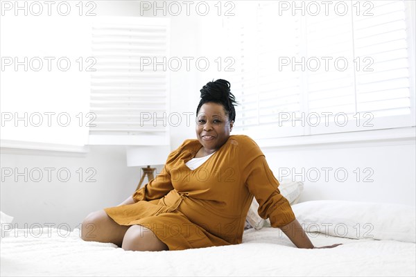 Portrait of smiling woman in orange dress sitting on bed