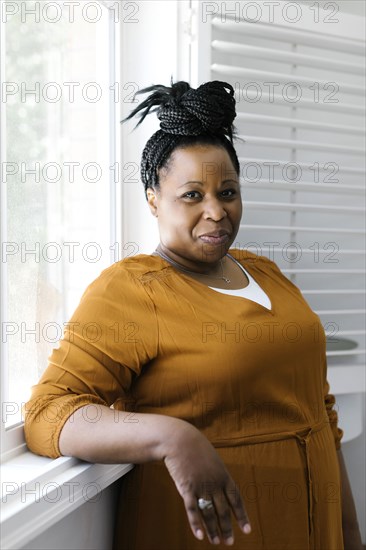 Portrait of smiling woman in orange dress standing by window