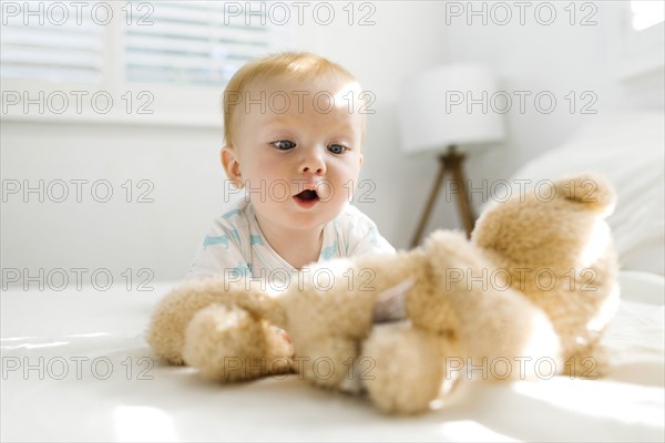 Baby boy (6-11 months) looking at teddy bear on bed