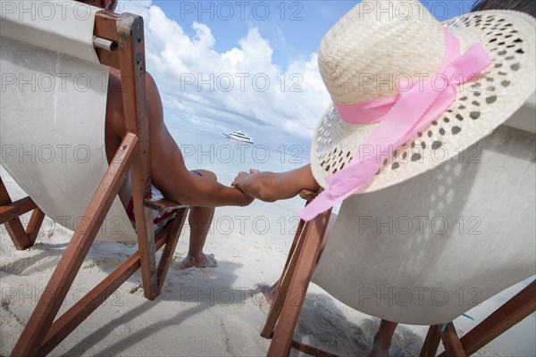 Rear view of couple on beach sitting on deckchairs and holding hands