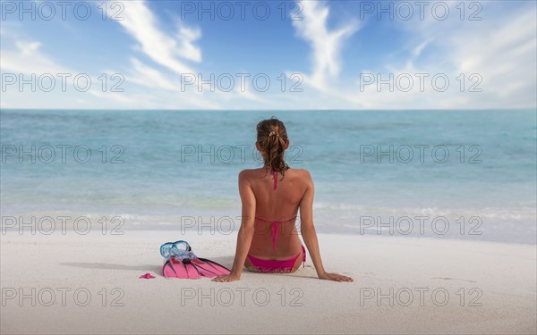Maldives, Rear view of woman in bikini sitting on beach