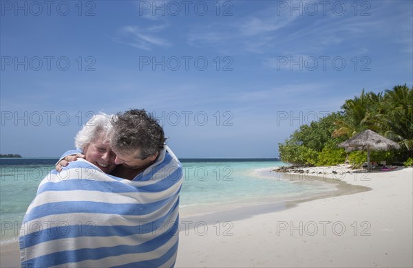 Indian Ocean, Maldives, Ari Atoll, Vilamendhoo Island, Happy couple wrapped in striped beach towel on tropical beach