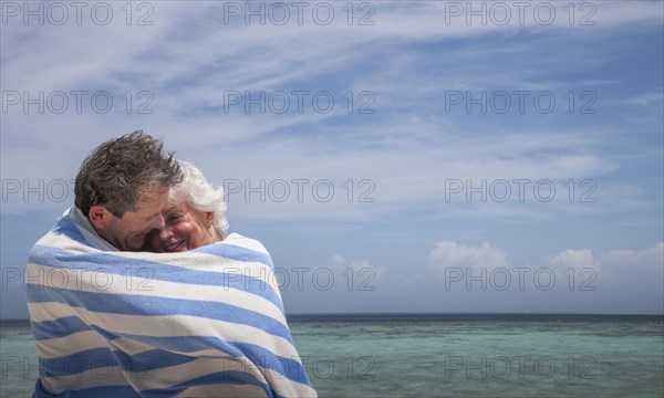 Indian Ocean, Maldives, Ari Atoll, Vilamendhoo Island, Happy couple wrapped in striped beach towel on tropical beach