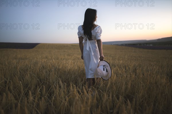 France, Young woman in white dress standing in cereal field