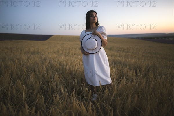 France, Young woman in white dress standing in cereal field