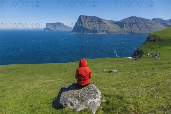 Denmark, Faroe Islands, Klaksvik, Trollanes, Woman sitting on rock and looking at ocean