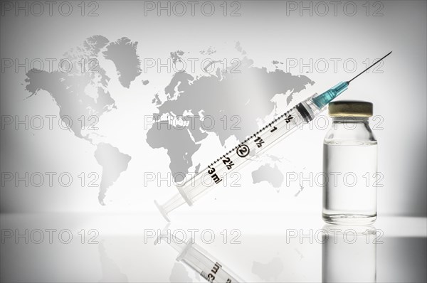 Studio shot of laboratory vial and syringe with world map in background