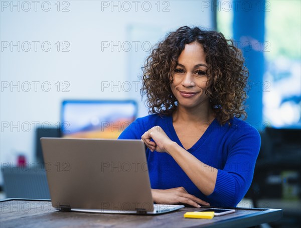 Portrait of smiling woman sitting at desk with laptop in office