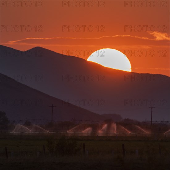 Irrigation equipment in field and sun setting behind mountain