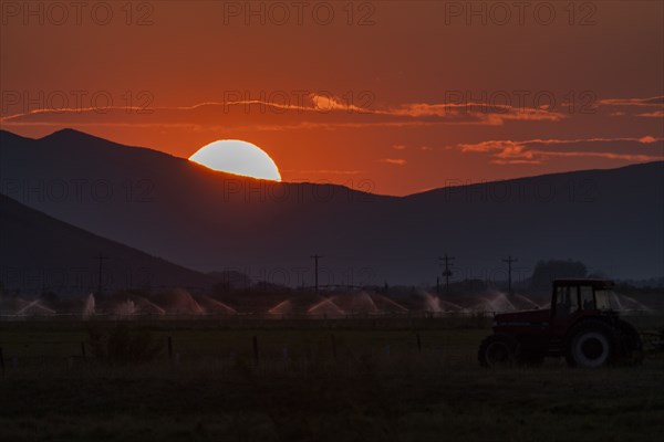 Irrigation equipment in field and sun setting behind mountain