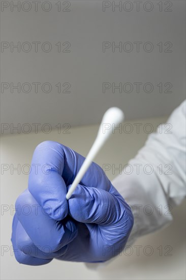 Gloved hand holds sterile swab for COVID testing