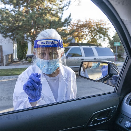 Female medical staff in protective clothing approaching car with coronavirus swab test