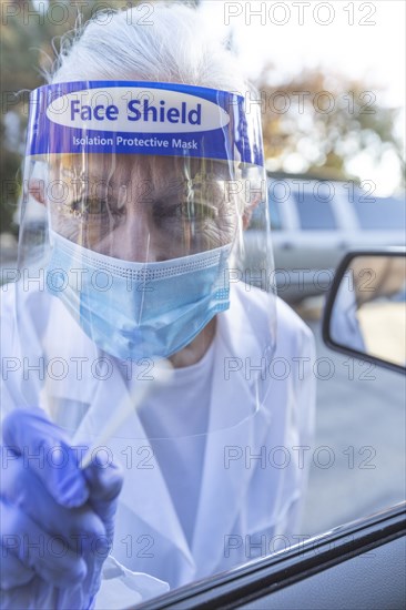 Female medical staff in protective clothing approaching car with coronavirus swab test