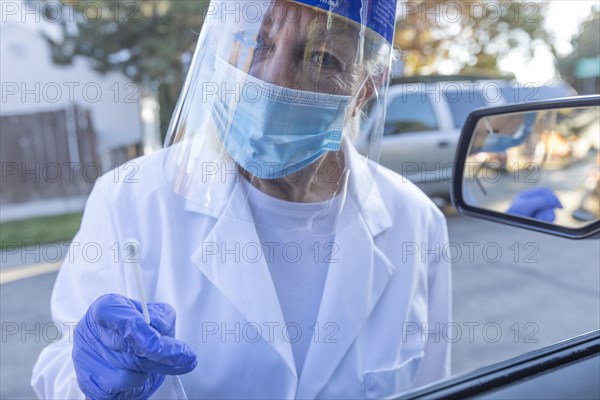 Female medical staff in protective clothing approaching car with coronavirus swab test