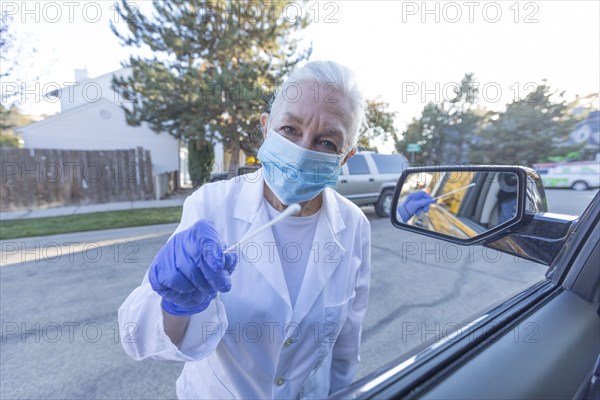 Female medical staff in protective clothing approaching car with coronavirus swab test