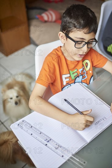 Boys (8-9) writing in notebook while learning at home during Covid-19 lockdown