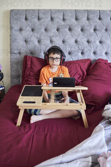 Boy (8-9) gaming on tablet while sitting in bed during weekend