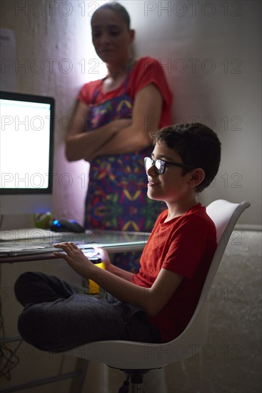 Mother watching son (8-9) during e-learning at home due to Covid-19 lockdown