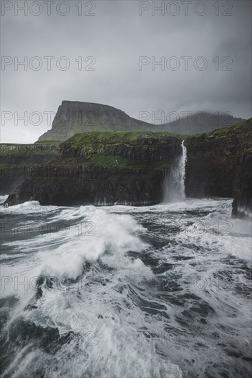 Coastline with Mulafossur Waterfall falling into Atlantic Ocean in stormy day