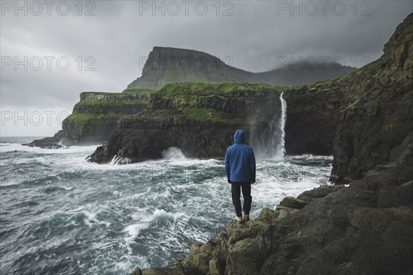 Man standing on cliff and looking at Mulafossur Waterfall day during storm