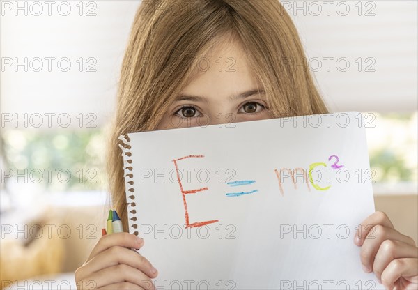 Girl (8-9) holding paper with Emc2 formula in front of face