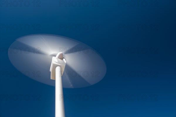 Low angle view of wind turbine spinning against blue sky