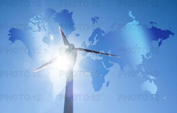 Wind turbine against blue sky and sun with world map in background