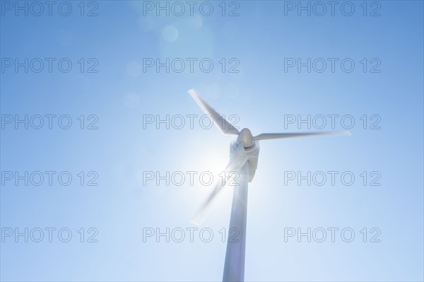 Low angle view of wind turbine against blue sky and sun