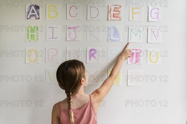 Rear view of girl (8-9) looking at alphabet on wall